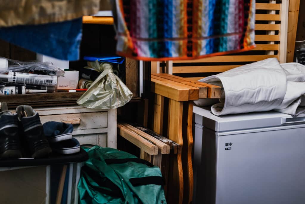 Rangement cabanon : outils, linge et mobilier en bois Rangement désordonné dans un cabanon : outils Fox, chaussures, linge blanc sur un congélateur blanc et un meuble en bois.